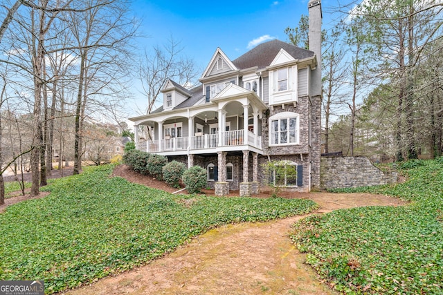 view of front of property featuring stone siding, covered porch, a chimney, and a balcony