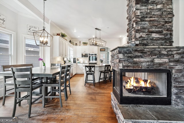 dining area featuring a multi sided fireplace, a chandelier, crown molding, and dark wood-style flooring