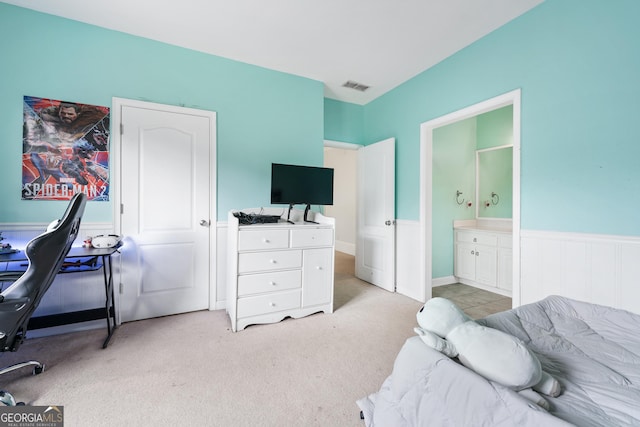 bedroom featuring ensuite bath, wainscoting, visible vents, and light carpet