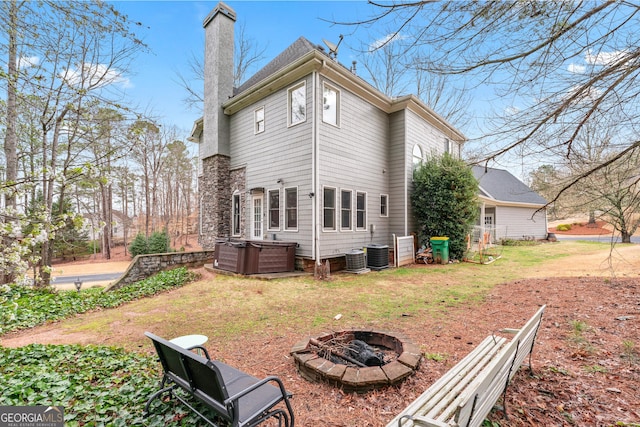 back of house featuring a hot tub, central air condition unit, an outdoor fire pit, a lawn, and a chimney