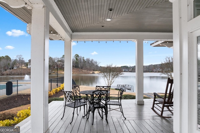 deck with outdoor dining area, a water view, and fence