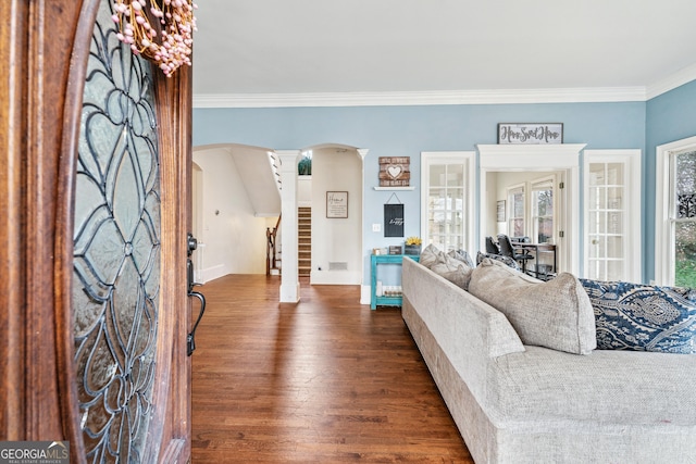 living room featuring stairway, ornate columns, arched walkways, dark wood-style flooring, and crown molding