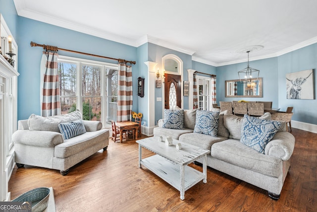 living room with a notable chandelier, ornamental molding, wood finished floors, decorative columns, and baseboards