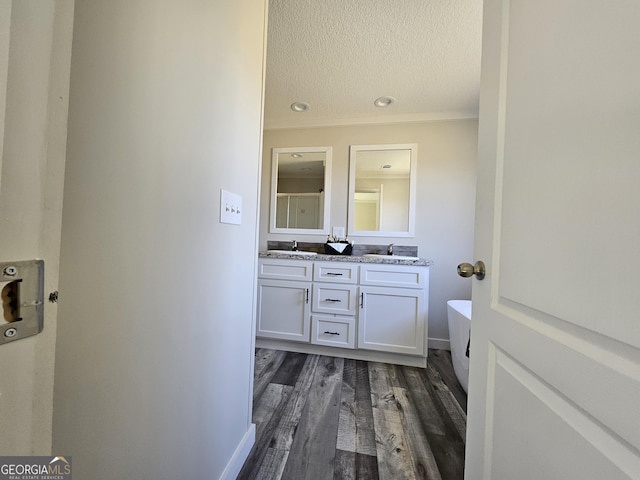 full bathroom with a sink, a textured ceiling, wood finished floors, double vanity, and a soaking tub