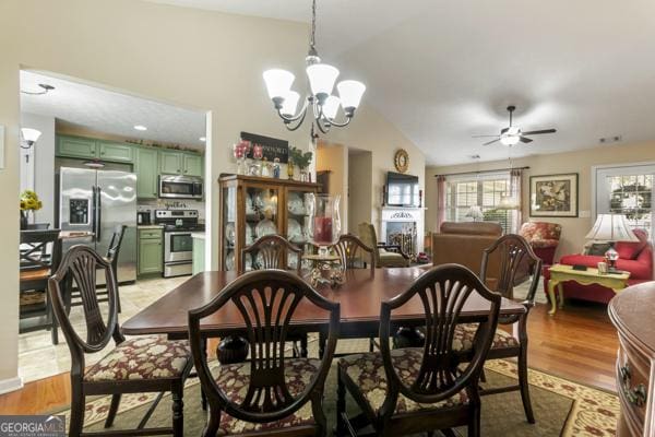 dining area with ceiling fan with notable chandelier, light wood-type flooring, and vaulted ceiling