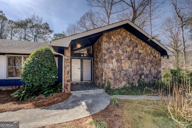 entrance to property with stone siding and roof with shingles