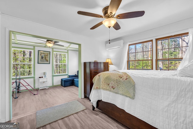 bedroom featuring multiple windows, a wall mounted AC, a ceiling fan, and wood finished floors