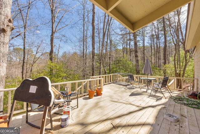 wooden terrace with a view of trees and outdoor dining area