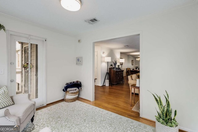 living area featuring visible vents, wood finished floors, crown molding, and a chandelier