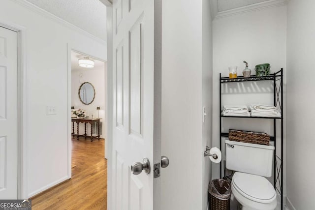 bathroom featuring toilet, a textured ceiling, wood finished floors, crown molding, and baseboards