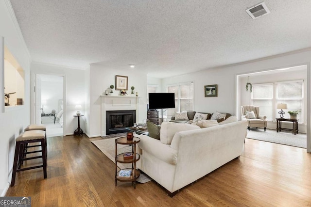 living room featuring visible vents, a textured ceiling, a fireplace with flush hearth, and wood finished floors