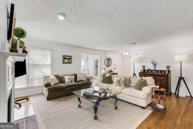 living area featuring a fireplace, visible vents, dark wood-style flooring, and a textured ceiling