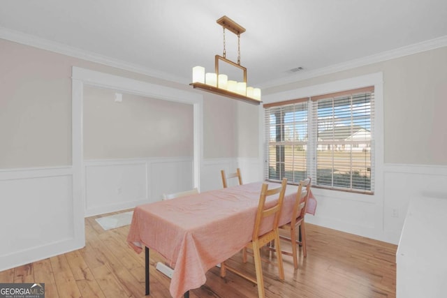 dining space featuring visible vents, light wood finished floors, an inviting chandelier, wainscoting, and crown molding