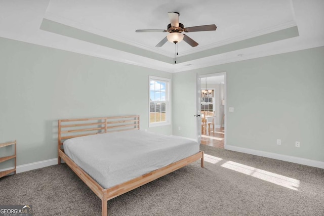 carpeted bedroom with ceiling fan with notable chandelier, baseboards, a tray ceiling, and ornamental molding