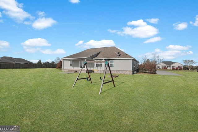 back of house with fence, a lawn, and a playground