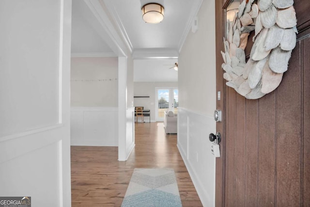 entryway featuring a wainscoted wall, wood finished floors, ornamental molding, and a decorative wall