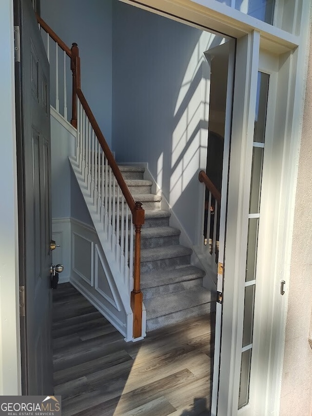 stairs with a wainscoted wall, wood finished floors, and a decorative wall