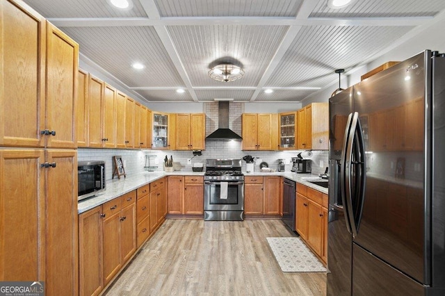 kitchen featuring light wood finished floors, tasteful backsplash, light countertops, appliances with stainless steel finishes, and wall chimney exhaust hood