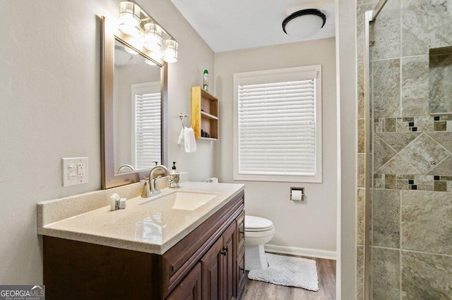 bathroom with a tile shower, toilet, vanity, and baseboards