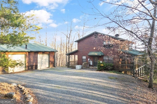 view of home's exterior with faux log siding, a detached garage, gravel driveway, central AC, and metal roof