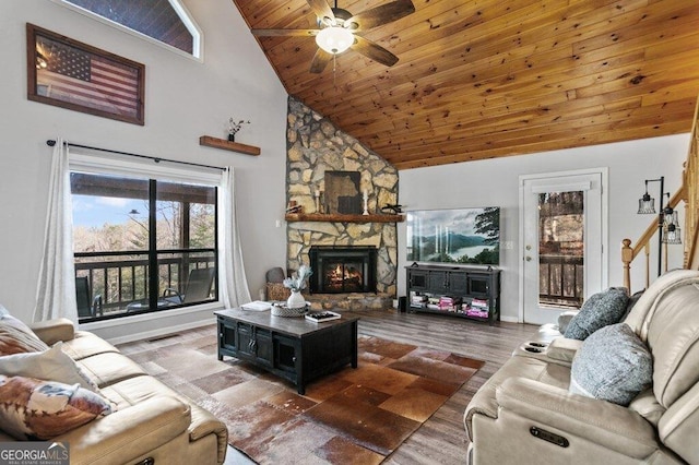 living room with a ceiling fan, wood finished floors, a stone fireplace, wooden ceiling, and baseboards