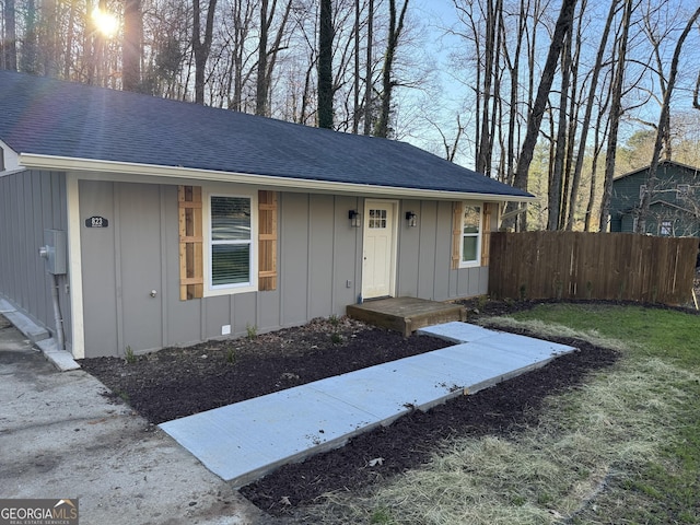 exterior space with roof with shingles, board and batten siding, and fence