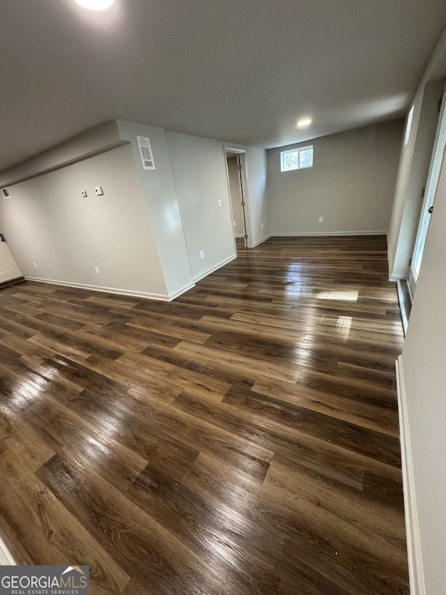 below grade area with dark wood-type flooring, visible vents, and baseboards