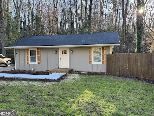 single story home featuring board and batten siding, a front lawn, and fence