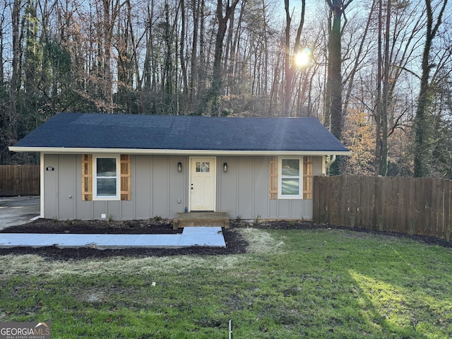 ranch-style house featuring board and batten siding, a front lawn, and fence