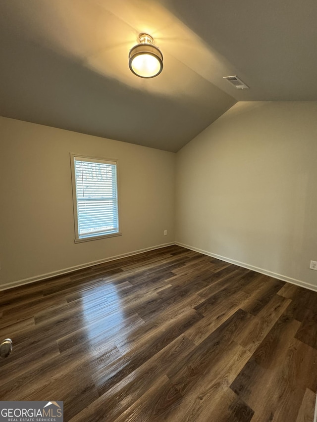 spare room featuring visible vents, baseboards, dark wood-style flooring, and vaulted ceiling