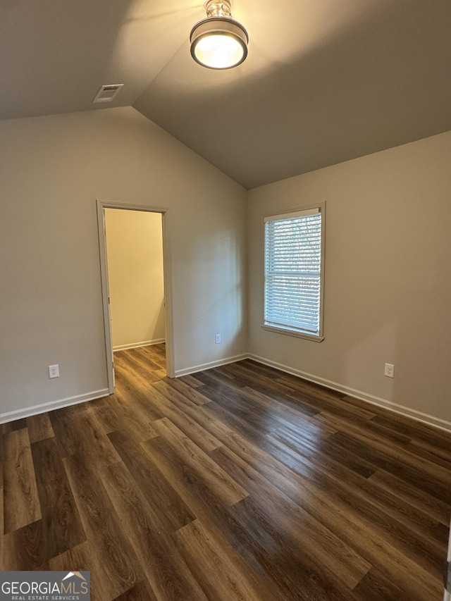 unfurnished room with vaulted ceiling, dark wood-style floors, visible vents, and baseboards