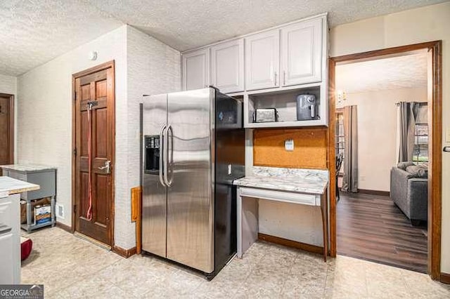 kitchen with baseboards, stainless steel fridge with ice dispenser, light countertops, a textured ceiling, and white cabinetry