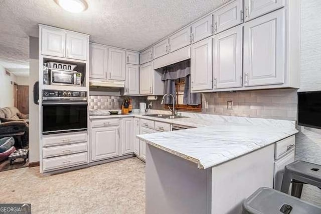 kitchen with a sink, backsplash, a textured ceiling, wall oven, and a peninsula