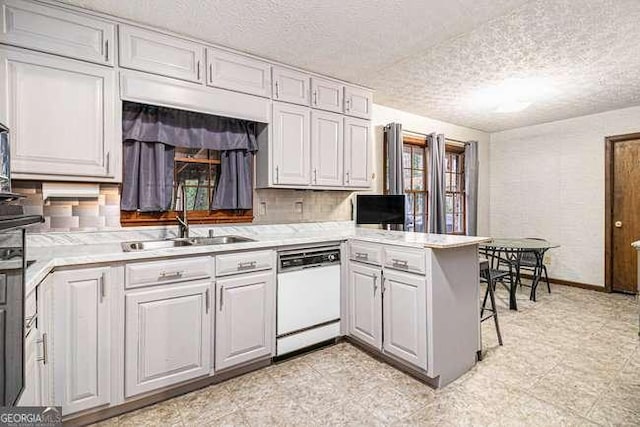 kitchen with light countertops, a peninsula, white dishwasher, a textured ceiling, and a sink