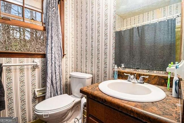 half bath with toilet, vanity, and wallpapered walls