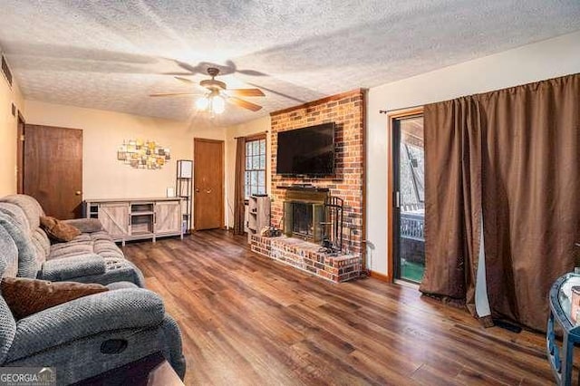 living area featuring a textured ceiling, a brick fireplace, wood finished floors, and a ceiling fan