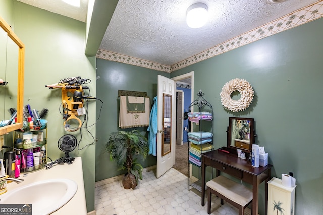 bathroom featuring a textured ceiling, tile patterned floors, baseboards, and a sink