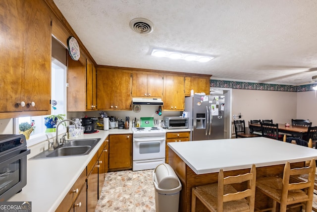 kitchen with under cabinet range hood, visible vents, appliances with stainless steel finishes, and brown cabinetry