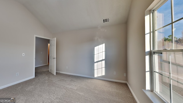 empty room featuring vaulted ceiling, carpet flooring, baseboards, and visible vents