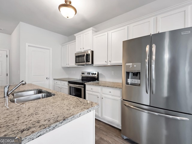 kitchen with dark wood-type flooring, a sink, white cabinetry, appliances with stainless steel finishes, and light stone countertops