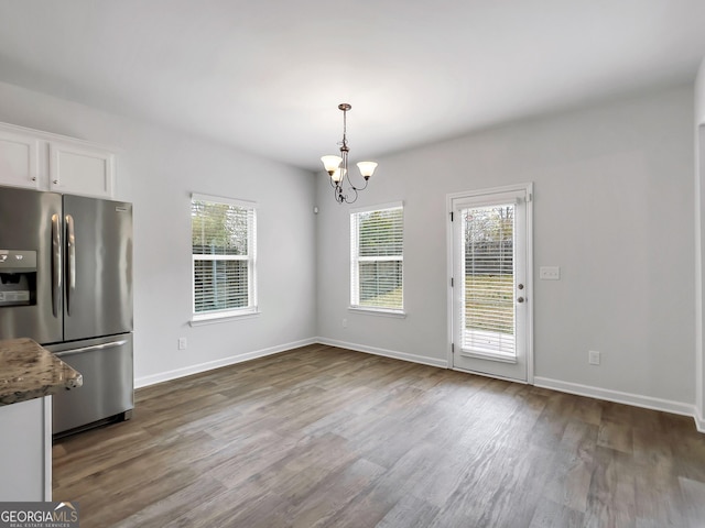 unfurnished dining area featuring a notable chandelier, plenty of natural light, baseboards, and dark wood-type flooring