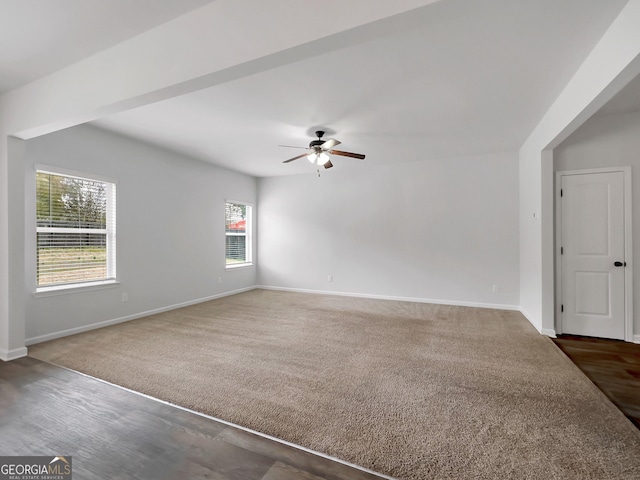 spare room featuring dark carpet, baseboards, dark wood-style flooring, and a ceiling fan