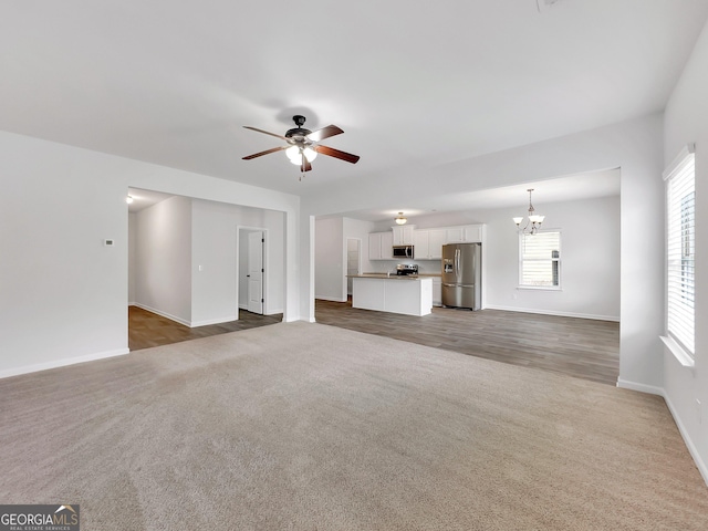 unfurnished living room featuring baseboards, carpet flooring, and ceiling fan with notable chandelier