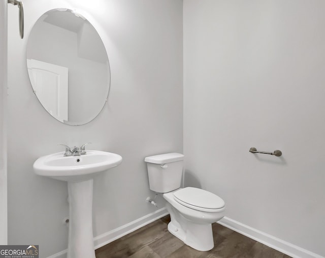 half bath featuring a sink, toilet, baseboards, and wood finished floors