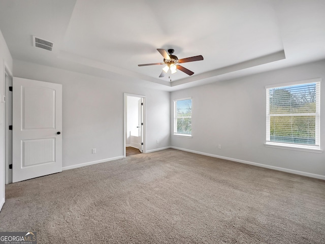 unfurnished bedroom with baseboards, visible vents, a tray ceiling, ensuite bathroom, and carpet flooring