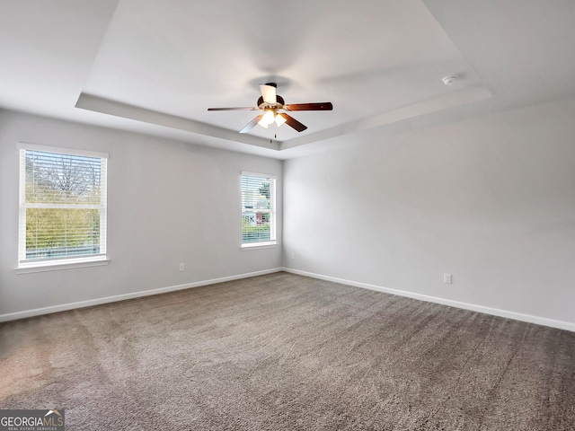 carpeted empty room with a ceiling fan, a raised ceiling, and baseboards