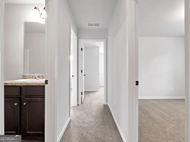 corridor with a sink, visible vents, baseboards, and carpet