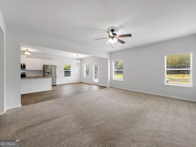 unfurnished living room featuring ceiling fan with notable chandelier, baseboards, and carpet floors