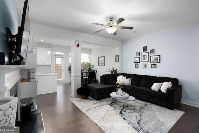 living room with a fireplace, baseboards, dark wood-type flooring, and ceiling fan