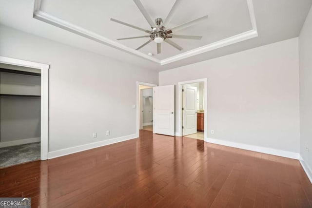 unfurnished bedroom featuring a tray ceiling, wood finished floors, and baseboards